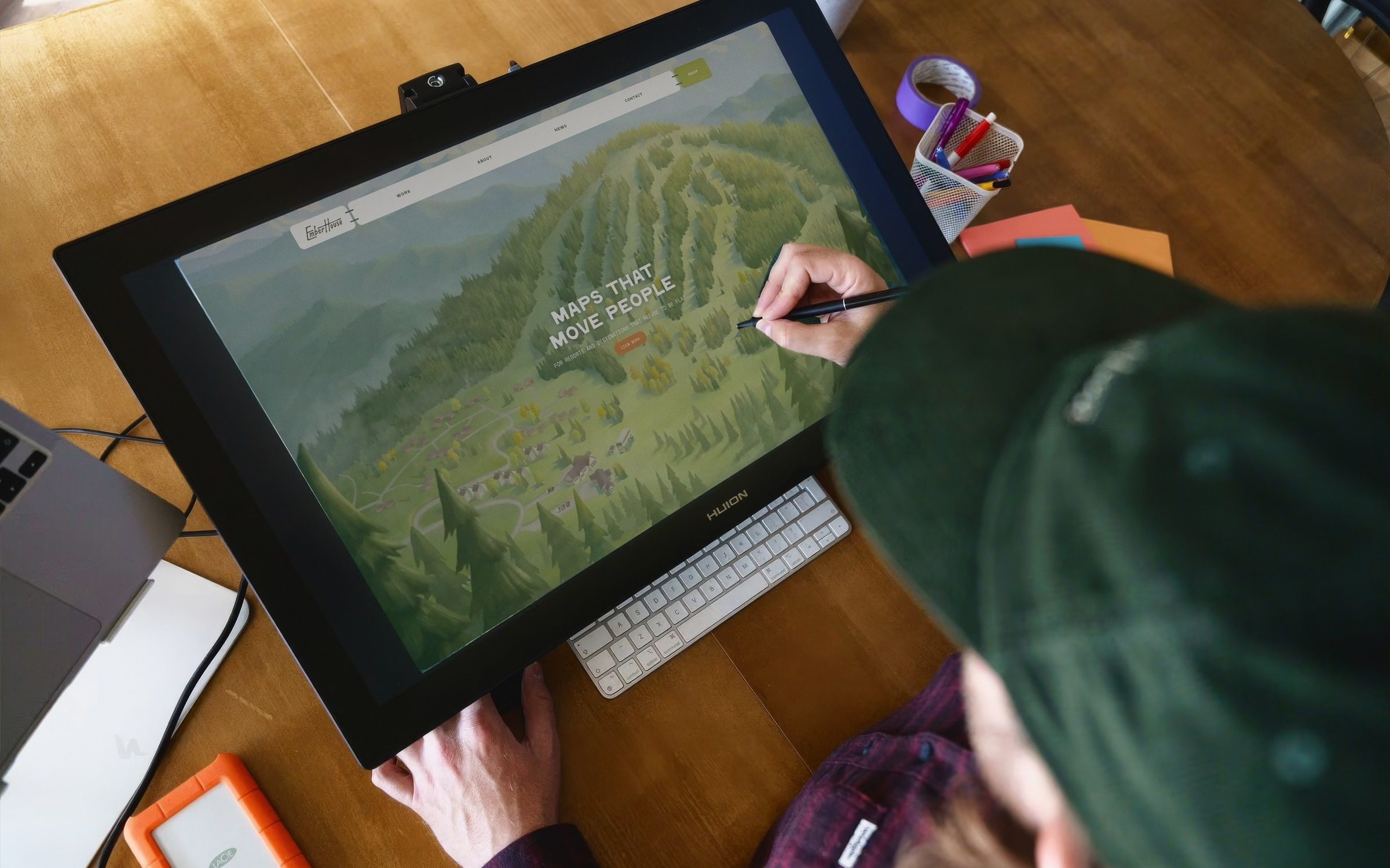 The Emberhouse homepage on a drawing tablet in a map studio, pen in hand over the summer map